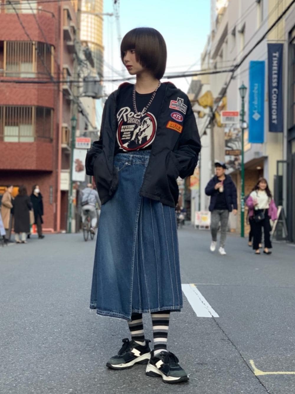 ブラック系のスニーカー、ブルー系のスカート、ブラック系のTシャツ/カットソーを着用したレディースの春コーディネートの1枚目の写真