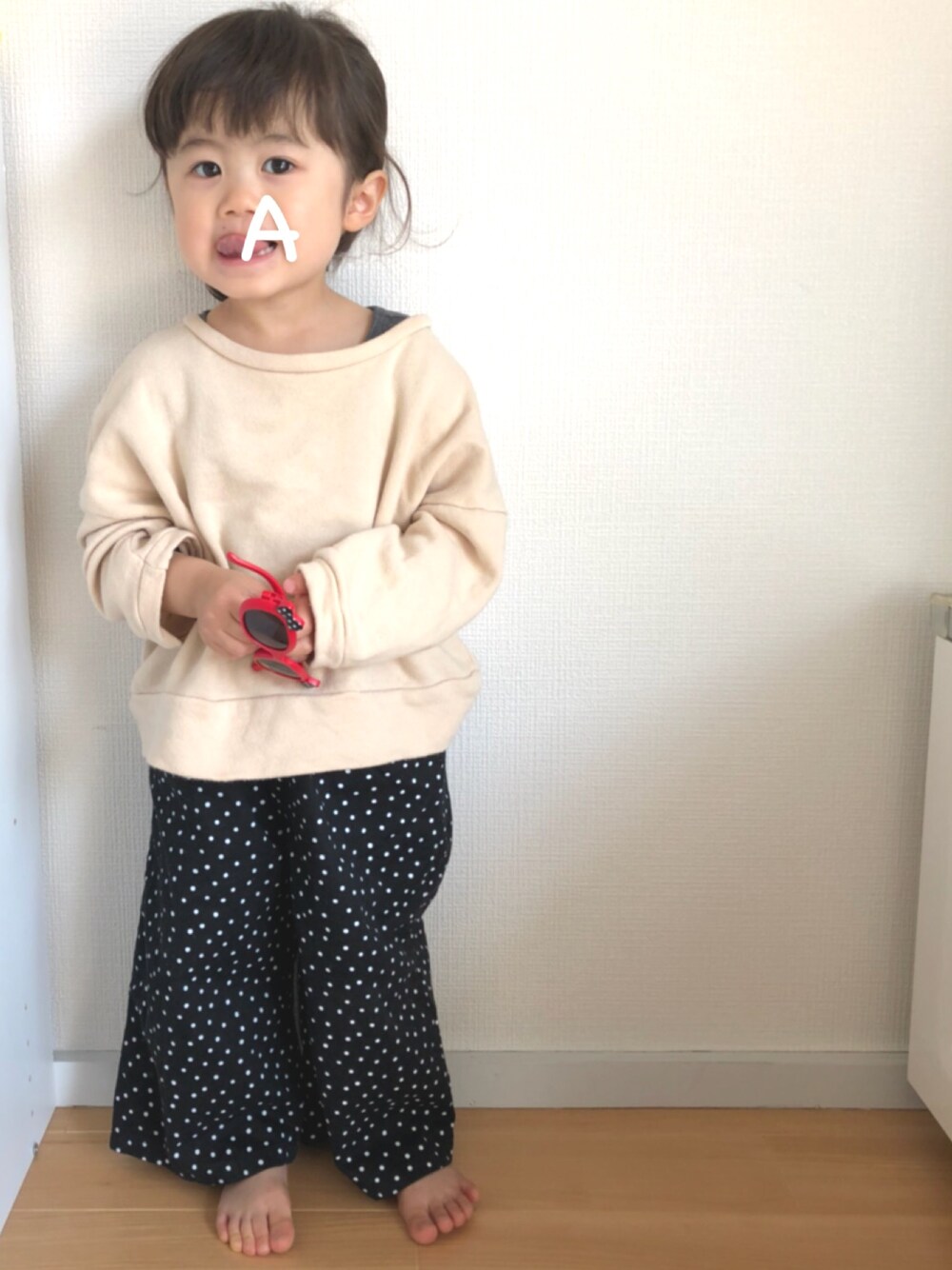 ベージュ系のトップス、ブラック系のパンツ、レッド系のサングラスを着用したキッズの春コーディネートの1枚目の写真