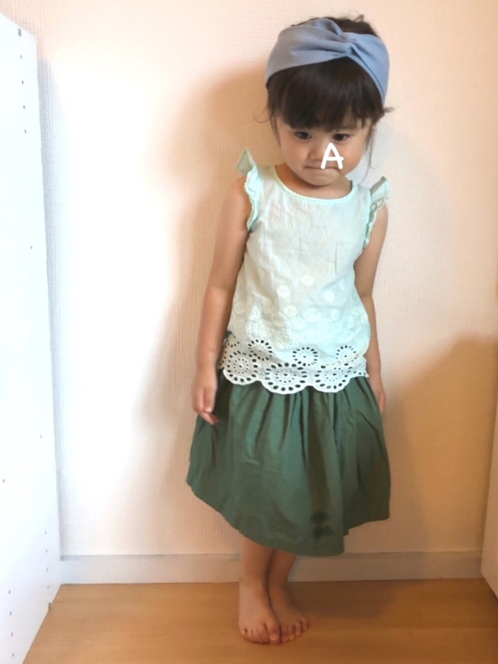 グリーン系のトップス、グリーン系のスカート、ブルー系のヘアバンドを着用したキッズの夏コーディネートの1枚目の写真