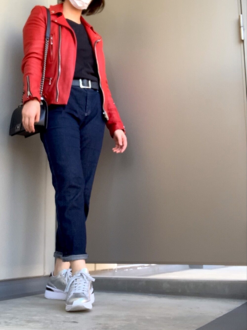 レッド系のライダースジャケット、シルバー系のスニーカー、ブルー系のデニムパンツを着用したレディースの秋コーディネートの1枚目の写真