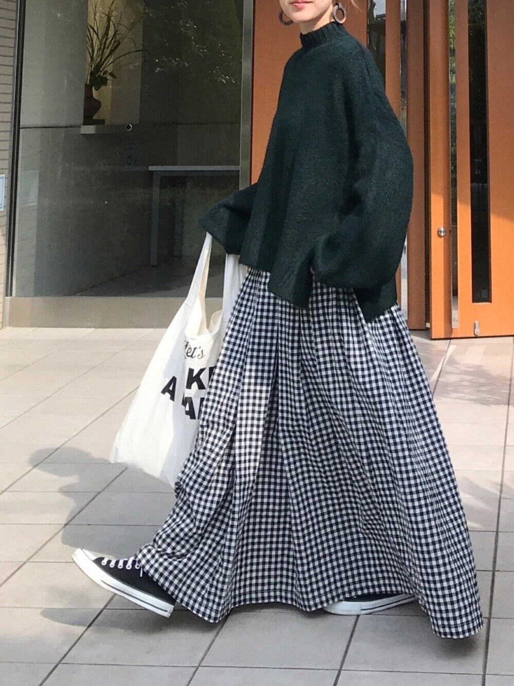 グリーン系のニット/セーター、ブラック系のスカート、ホワイト系のトートバッグを着用したレディースの秋コーディネートの1枚目の写真