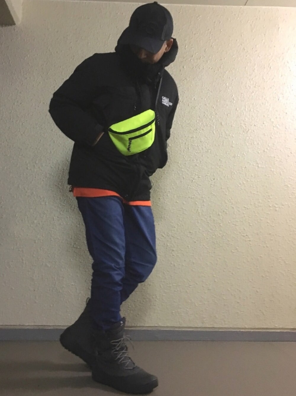 イエロー系のボディバッグ/ウエストポーチ、オレンジ系のスウェット、グレー系のブーツを着用したメンズの冬コーディネートの1枚目の写真