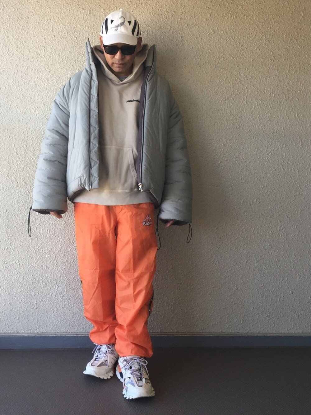 グレー系のダウンジャケット/コート、オレンジ系のパンツ、ホワイト系のスニーカーを着用したメンズの冬コーディネートの1枚目の写真