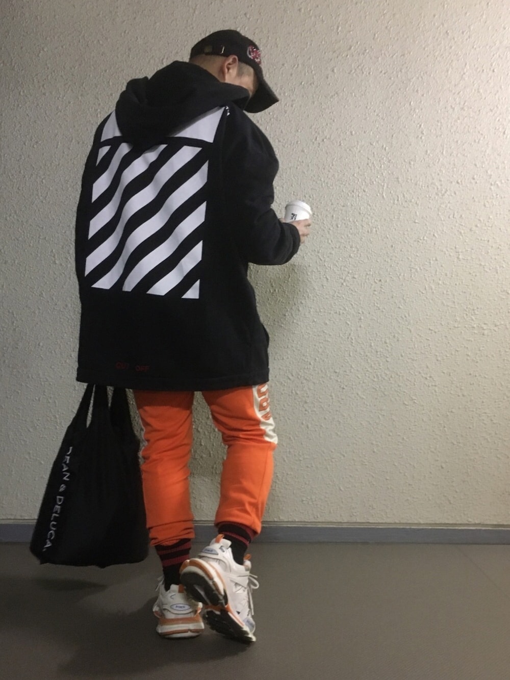 ブラック系のパーカー、オレンジ系のパンツ、ホワイト系のスニーカーを着用したメンズの冬コーディネートの1枚目の写真