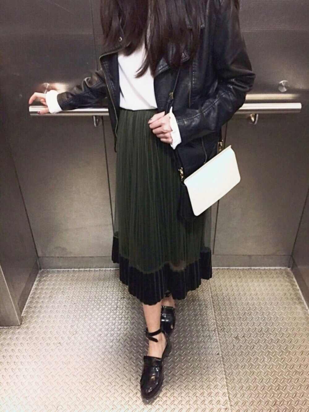 ホワイト系のトートバッグ、グリーン系のスカート、ブラック系のライダースジャケットを着用したレディースの春コーディネートの1枚目の写真