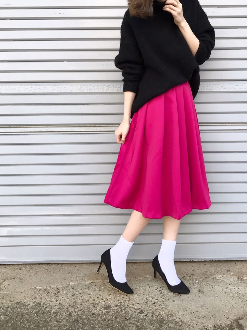 ピンク系のスカート、ブラック系のパンプス、ブラック系のニット/セーターを着用したレディースの冬コーディネートの1枚目の写真