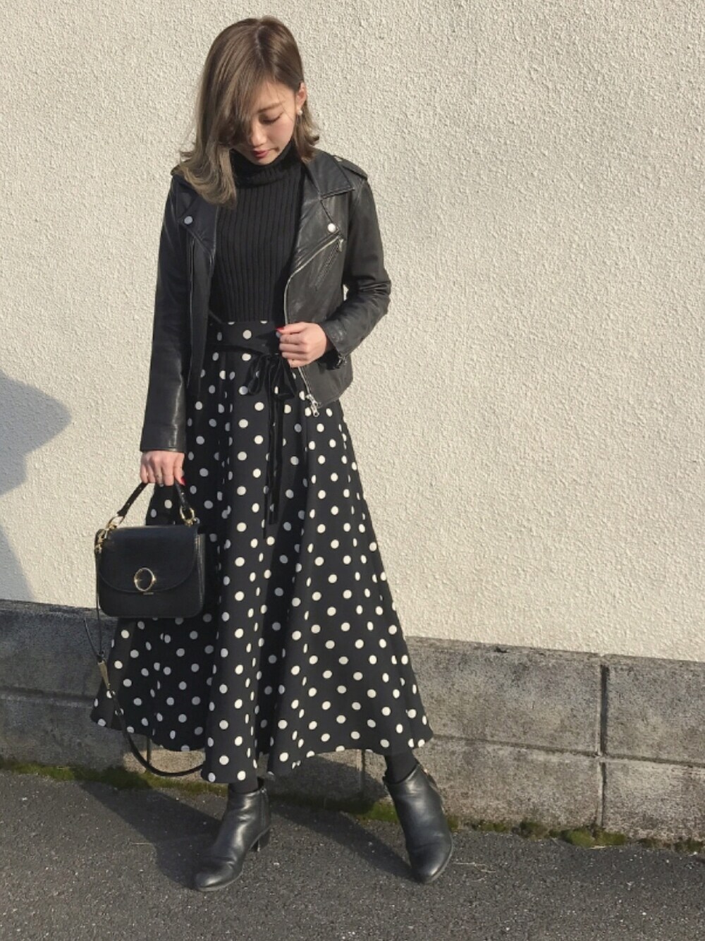 ブラック系のスカート、ブラック系のライダースジャケット、ブラック系のハンドバッグを着用したレディースの冬コーディネートの1枚目の写真