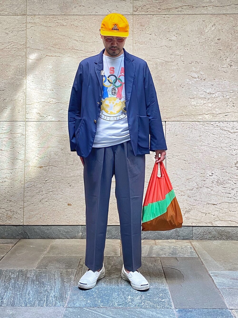 グレー系のその他パンツ、ホワイト系のスニーカー、オレンジ系のエコバッグ/サブバッグを着用したメンズの春コーディネートの1枚目の写真