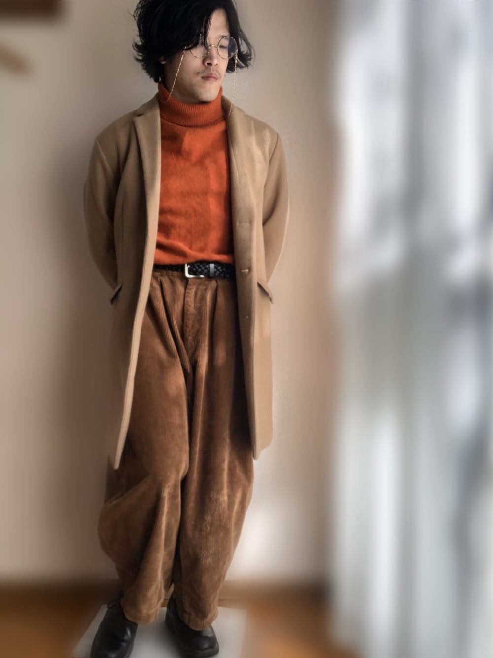 ベージュ系のチェスターコート、オレンジ系のニット/セーター、ブラウン系のパンツを着用したメンズの冬コーディネートの1枚目の写真