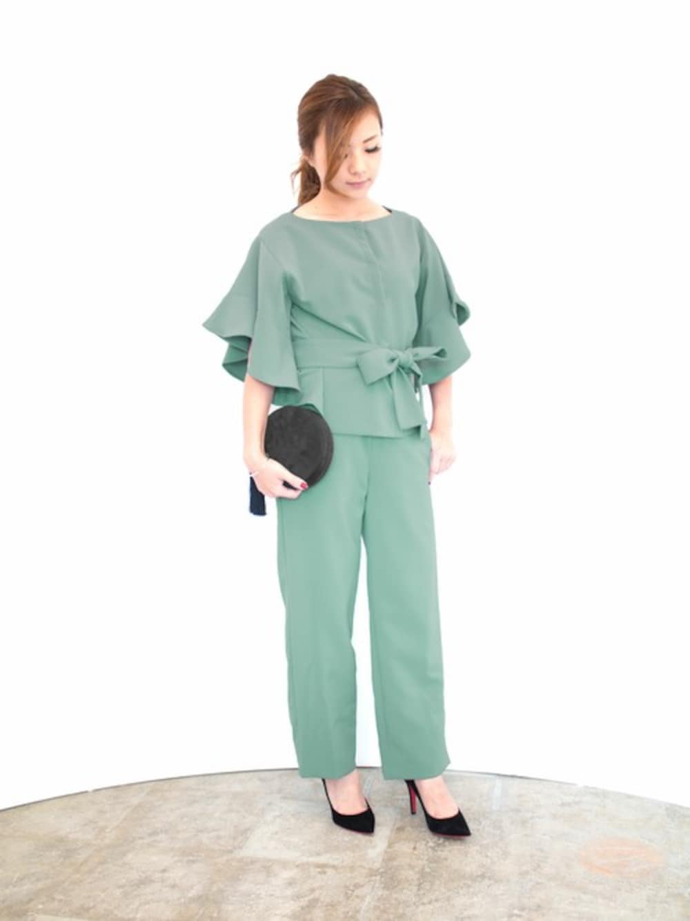 グレー系のパンツドレス、ブラック系のクラッチバッグを着用したレディースの秋コーディネートの1枚目の写真