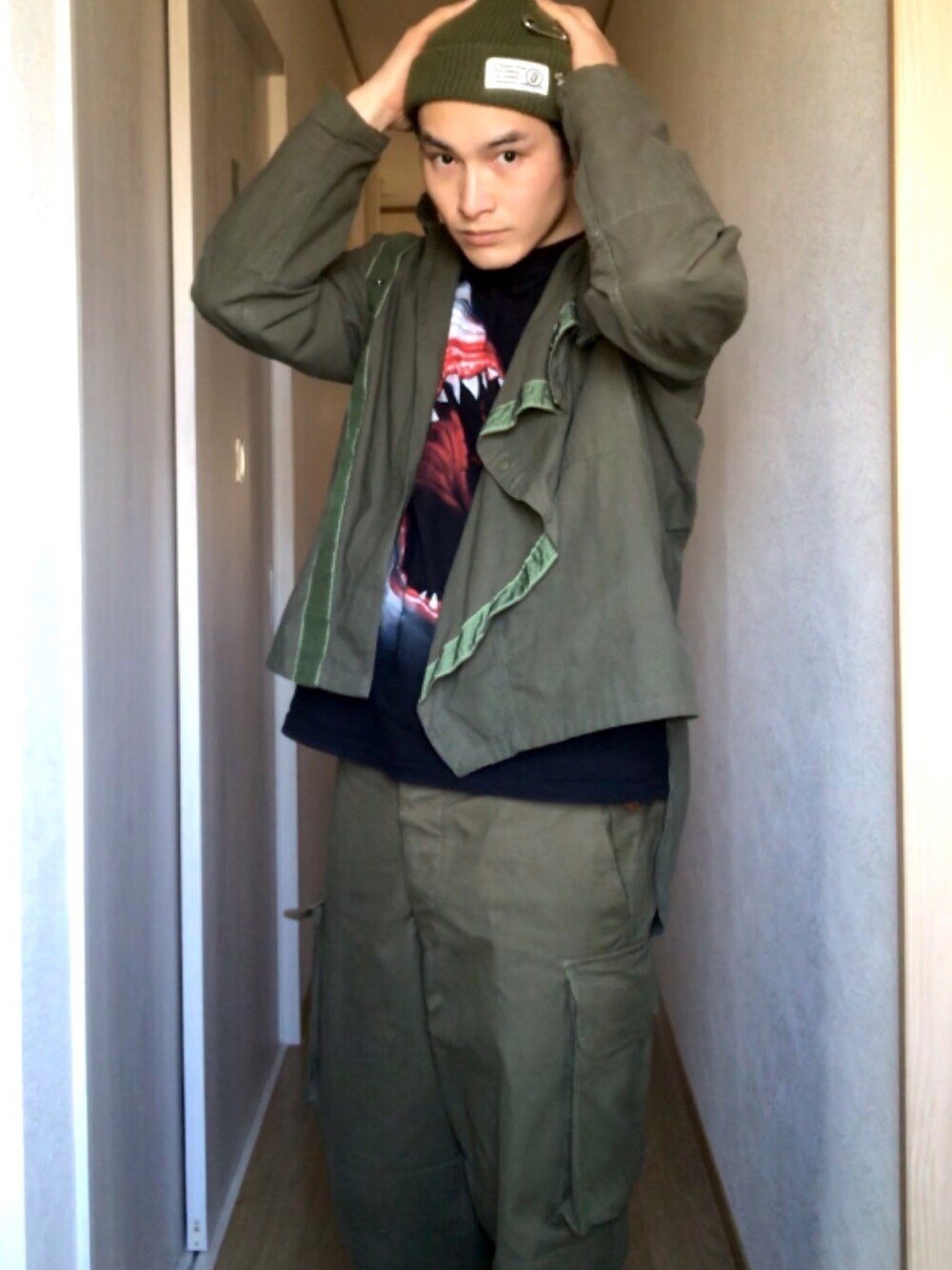 グリーン系のミリタリージャケット、グリーン系のカーゴパンツ、ブラック系のTシャツ/カットソーを着用したメンズの春コーディネートの1枚目の写真