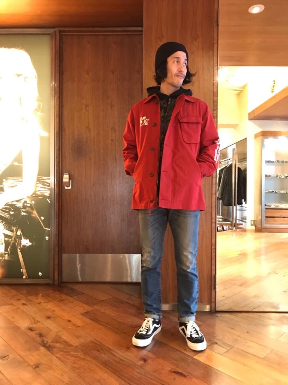 ブルー系のデニムパンツ、ブラック系のニット/セーター、レッド系のミリタリージャケットを着用したメンズの冬コーディネートの1枚目の写真