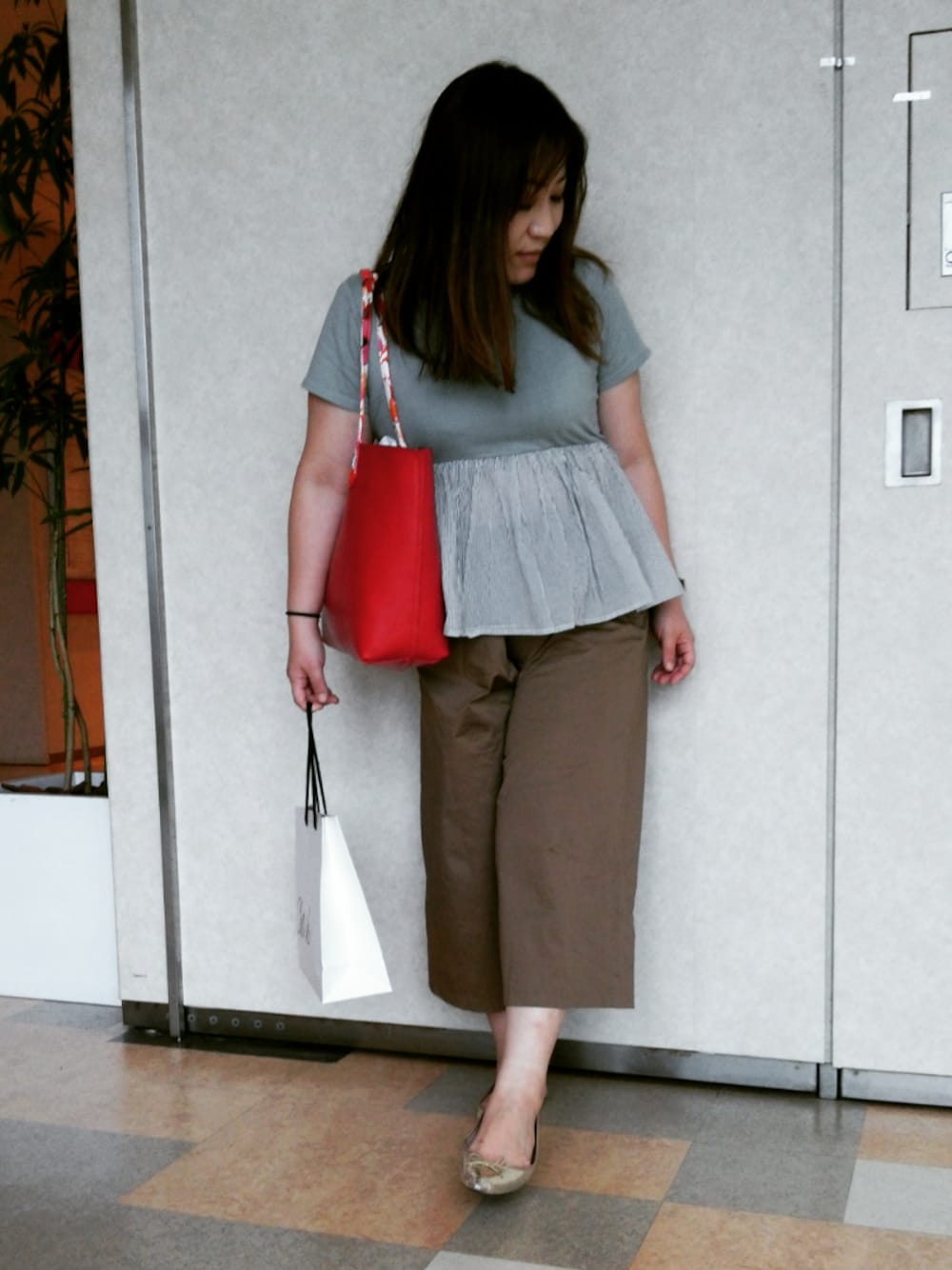 レッド系のトートバッグ、ブラウン系のパンツ、シルバー系のパンプスを着用したレディースの夏コーディネートの1枚目の写真