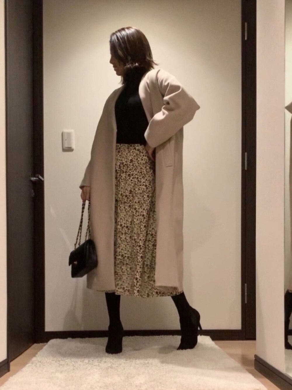 ベージュ系のノーカラーコート、ブラック系のニット/セーター、ホワイト系のスカートを着用したレディースの冬コーディネートの1枚目の写真