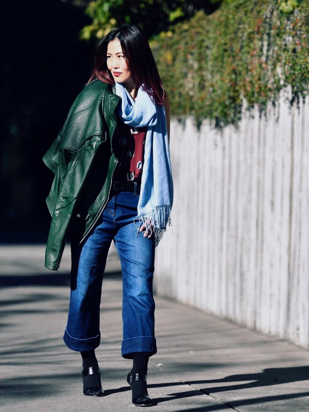 グリーン系のライダースジャケット、ブルー系のデニムパンツ、ブラック系のサンダルを着用したレディースの春コーディネートの1枚目の写真