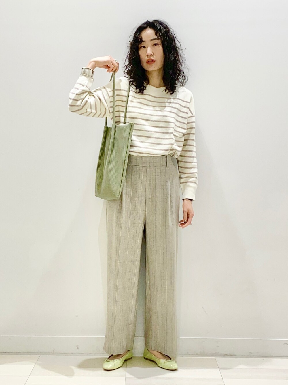 グリーン系のトートバッグ、ベージュ系のトップス、ブラウン系のその他パンツを着用したレディースの冬コーディネートの1枚目の写真