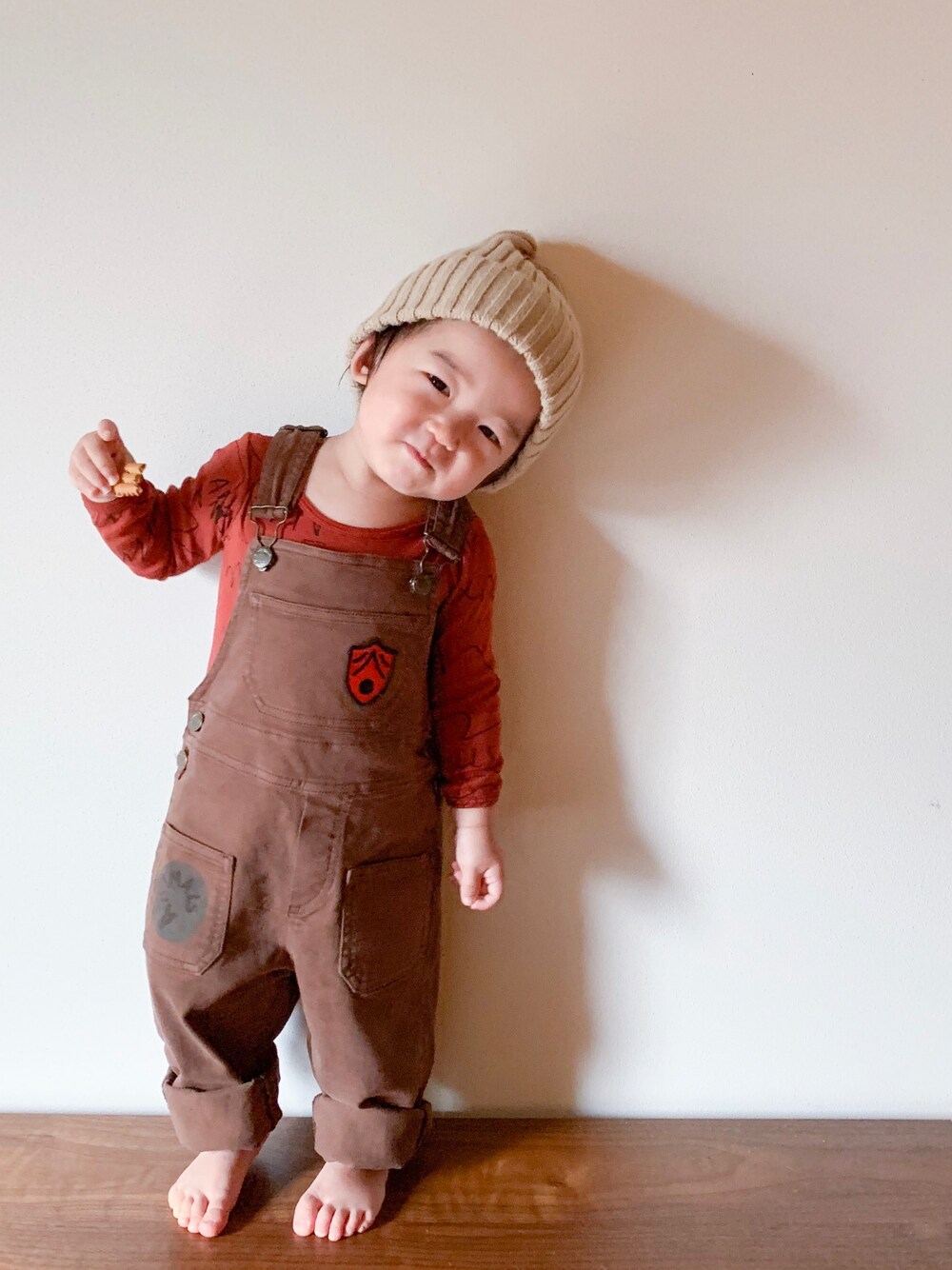 ブラウン系のサロペット/オーバーオール、ベージュ系のニットキャップ/ビーニー、レッド系のロンパースを着用したキッズの秋コーディネートの1枚目の写真