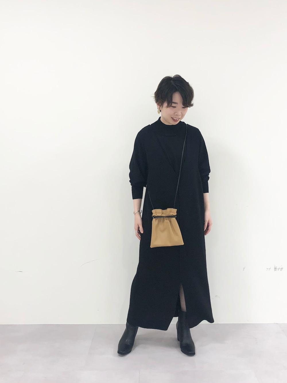 ブラック系のジャンパースカート、イエロー系のハンドバッグ、ブラック系のブーツを着用したレディースの冬コーディネートの1枚目の写真
