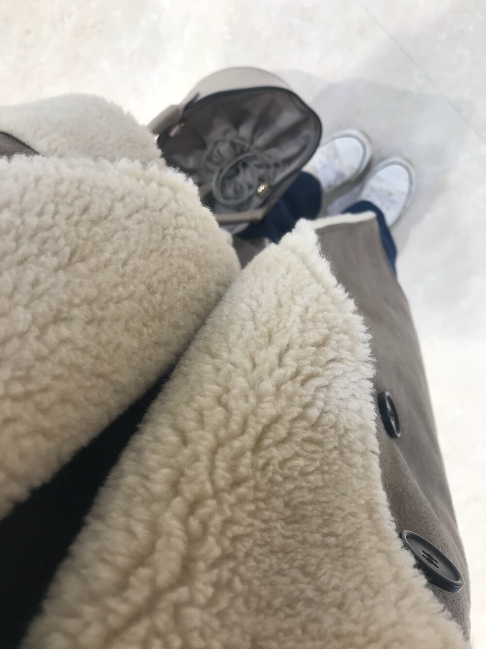 ベージュ系のムートンコート、ベージュ系のショルダーバッグ、ブルー系のデニムパンツを着用したレディースの冬コーディネートの1枚目の写真