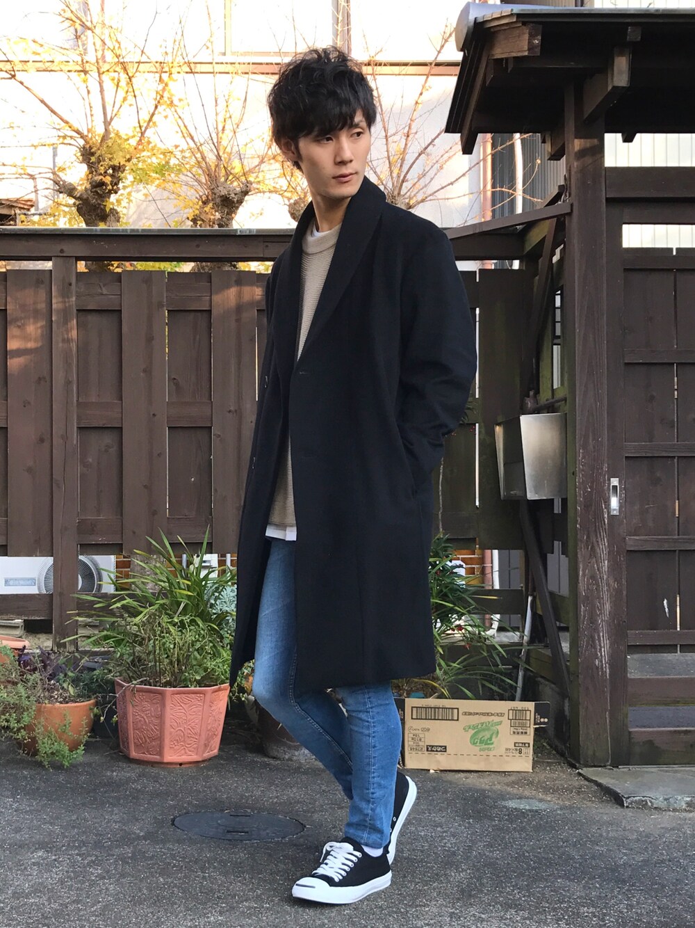 ブラック系のチェスターコート、ベージュ系のニット/セーター、ホワイト系のTシャツ/カットソーを着用したメンズの冬コーディネートの1枚目の写真