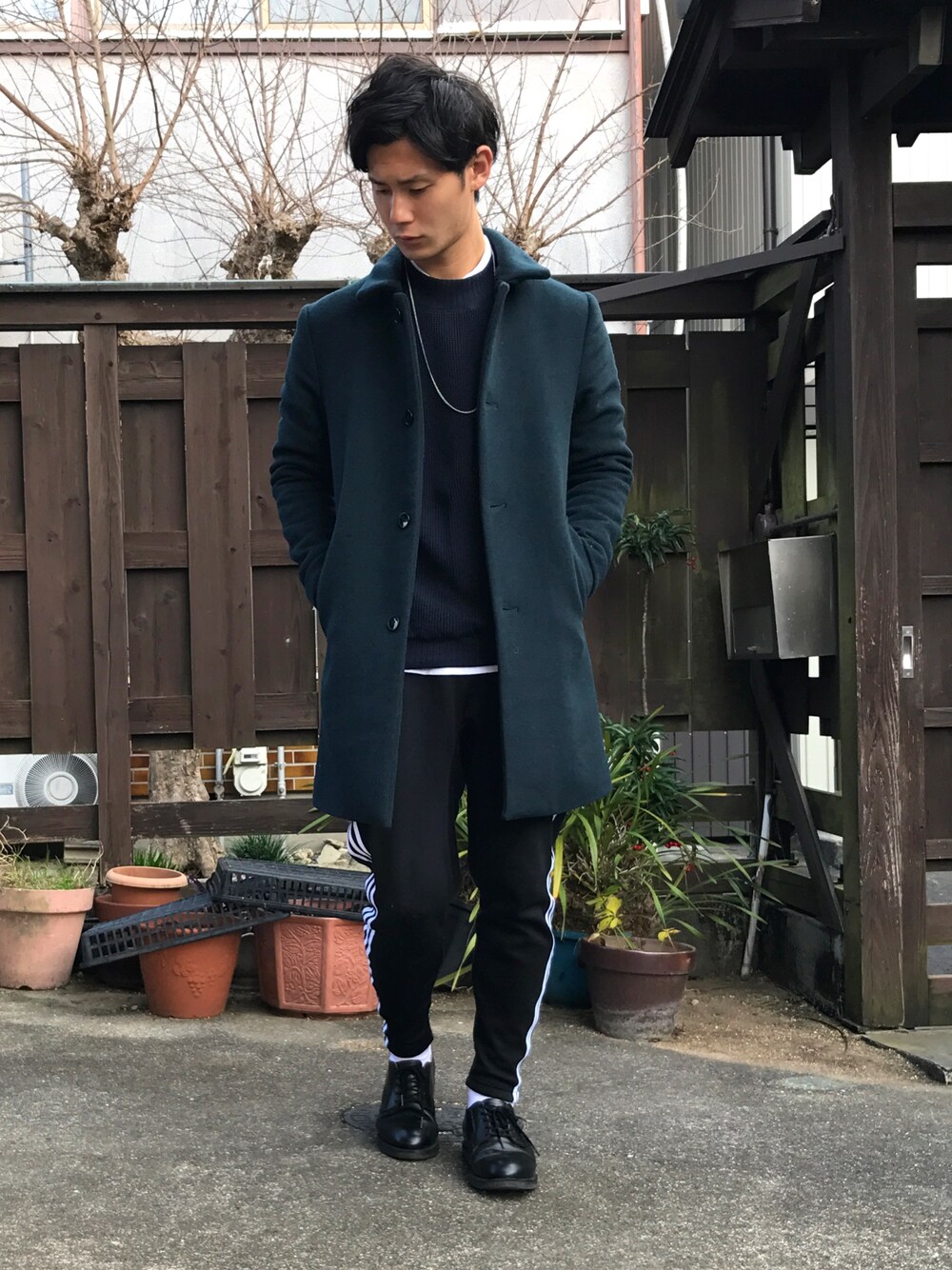グリーン系のステンカラーコート、ブルー系のニット/セーター、ホワイト系のTシャツ/カットソーを着用したメンズの冬コーディネートの1枚目の写真