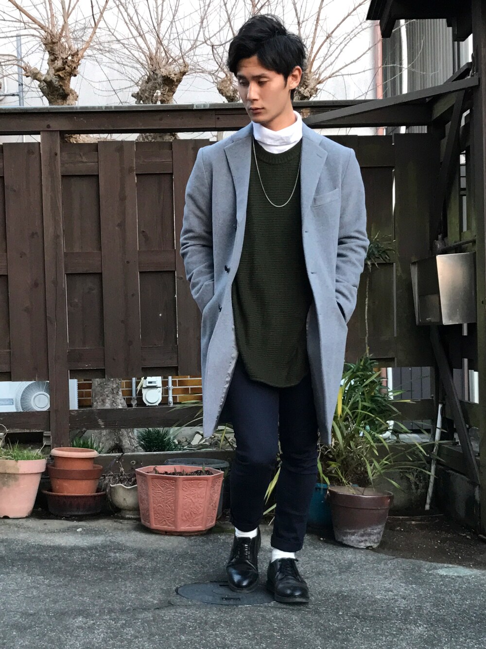 グレー系のチェスターコート、ホワイト系のTシャツ/カットソー、グリーン系のニット/セーターを着用したメンズの冬コーディネートの1枚目の写真