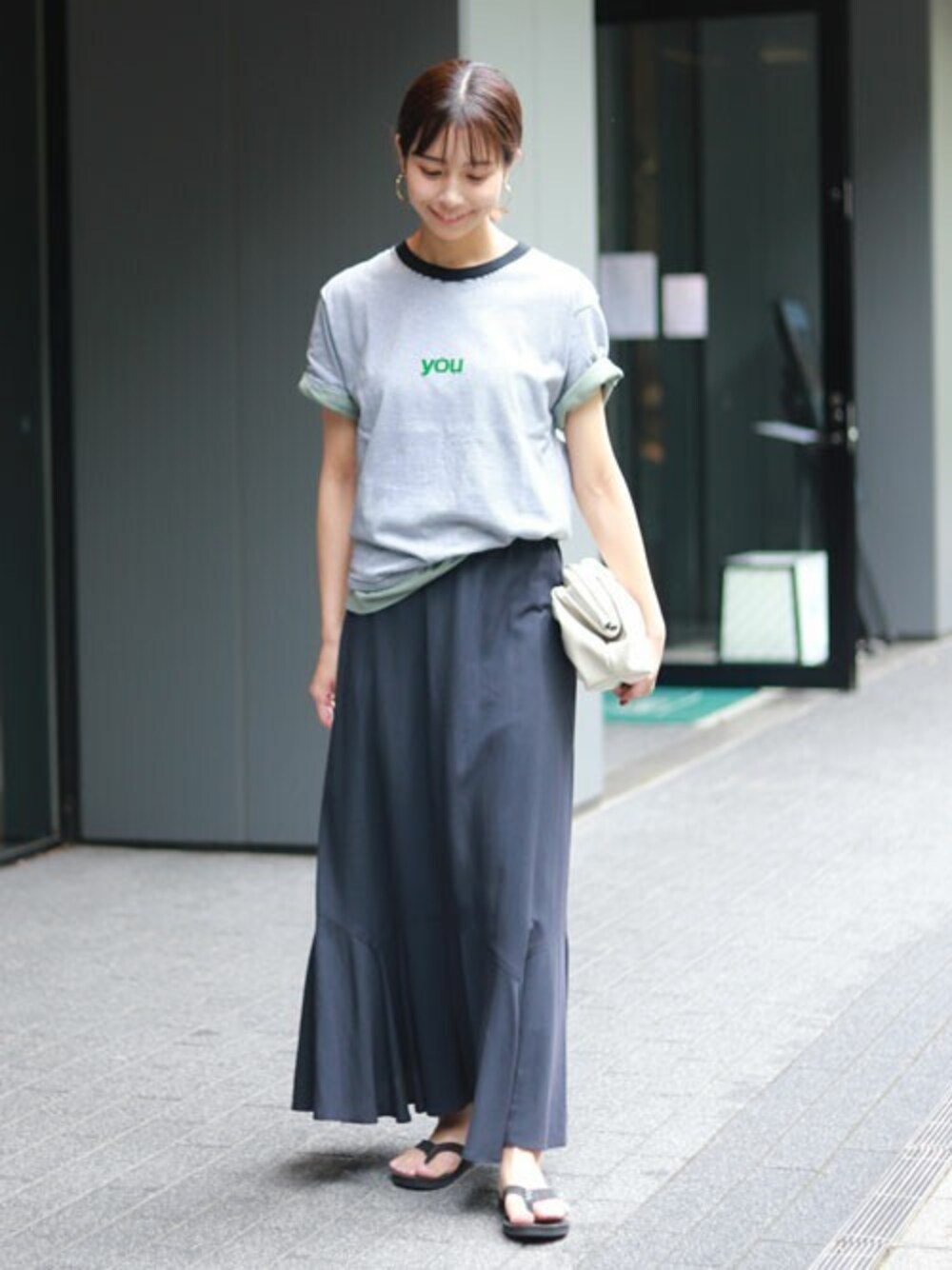 グレー系のスカート、ブラック系のサンダル、ブラック系のTシャツ/カットソーを着用したレディースの夏コーディネートの1枚目の写真