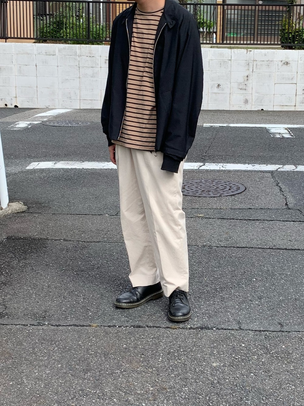 グレー系のブルゾン、ベージュ系のトップス、ホワイト系のチノパンツを着用したメンズの秋コーディネートの1枚目の写真