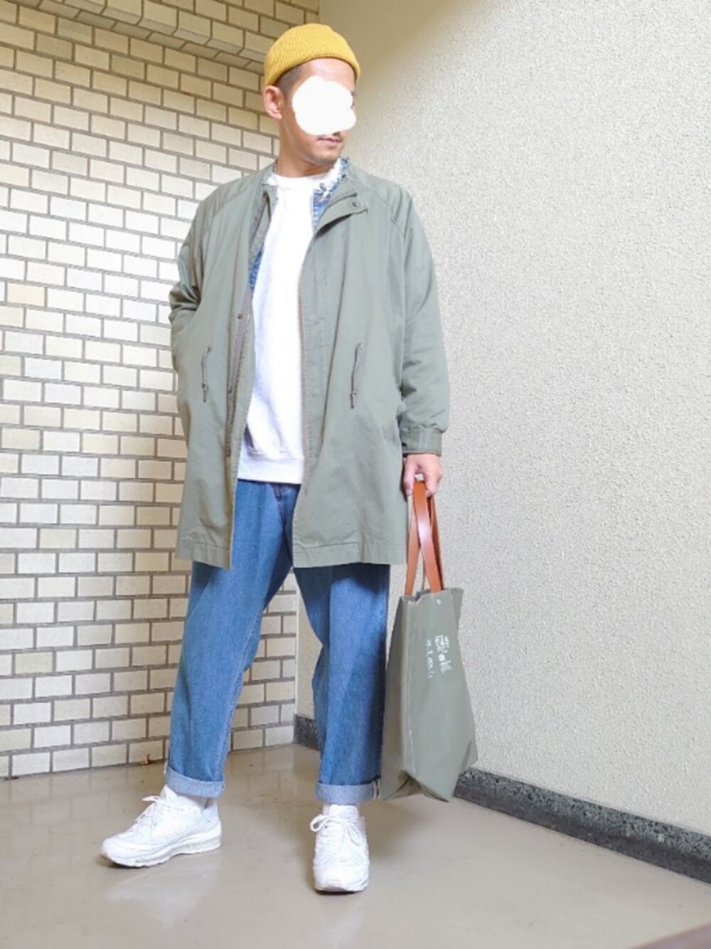グリーン系のトートバッグ、ブルー系のデニムパンツ、ホワイト系のスニーカーを着用したメンズの冬コーディネートの1枚目の写真