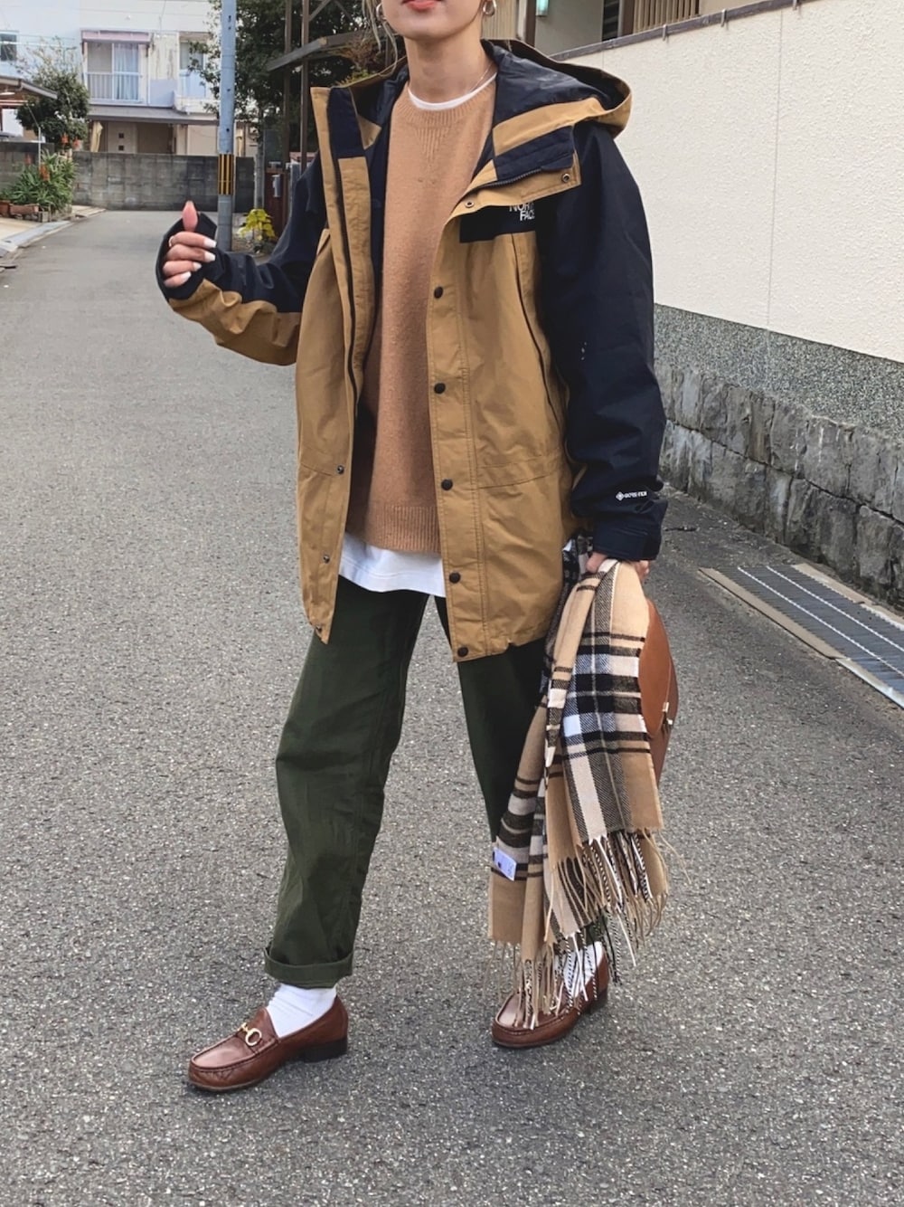 ベージュ系のマウンテンパーカー、ブラック系のニット/セーター、グリーン系のパンツを着用したレディースの冬コーディネートの1枚目の写真