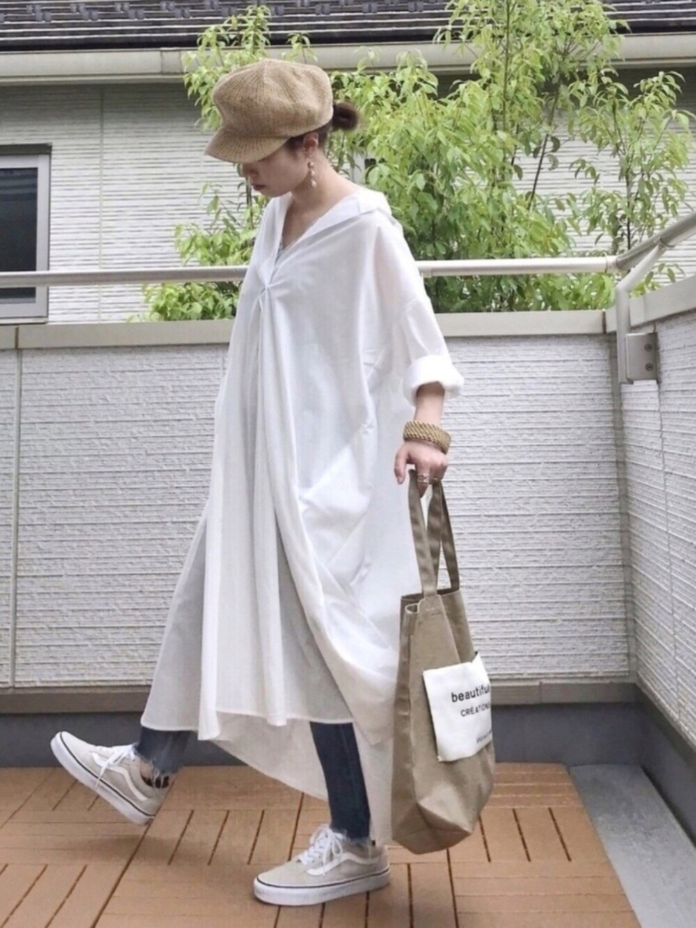 ホワイト系のシャツワンピース、ブルー系のデニムパンツ、ベージュ系のトートバッグを着用したレディースの春コーディネートの1枚目の写真