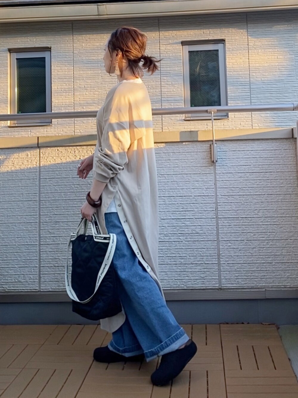 ベージュ系のワンピース、ブルー系のデニムパンツ、ブラック系のショルダーバッグを着用したレディースの春コーディネートの1枚目の写真