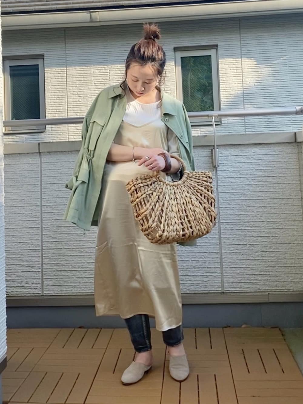 ベージュ系のワンピース、グリーン系のミリタリージャケット、ブラック系のデニムパンツを着用したレディースの春コーディネートの1枚目の写真