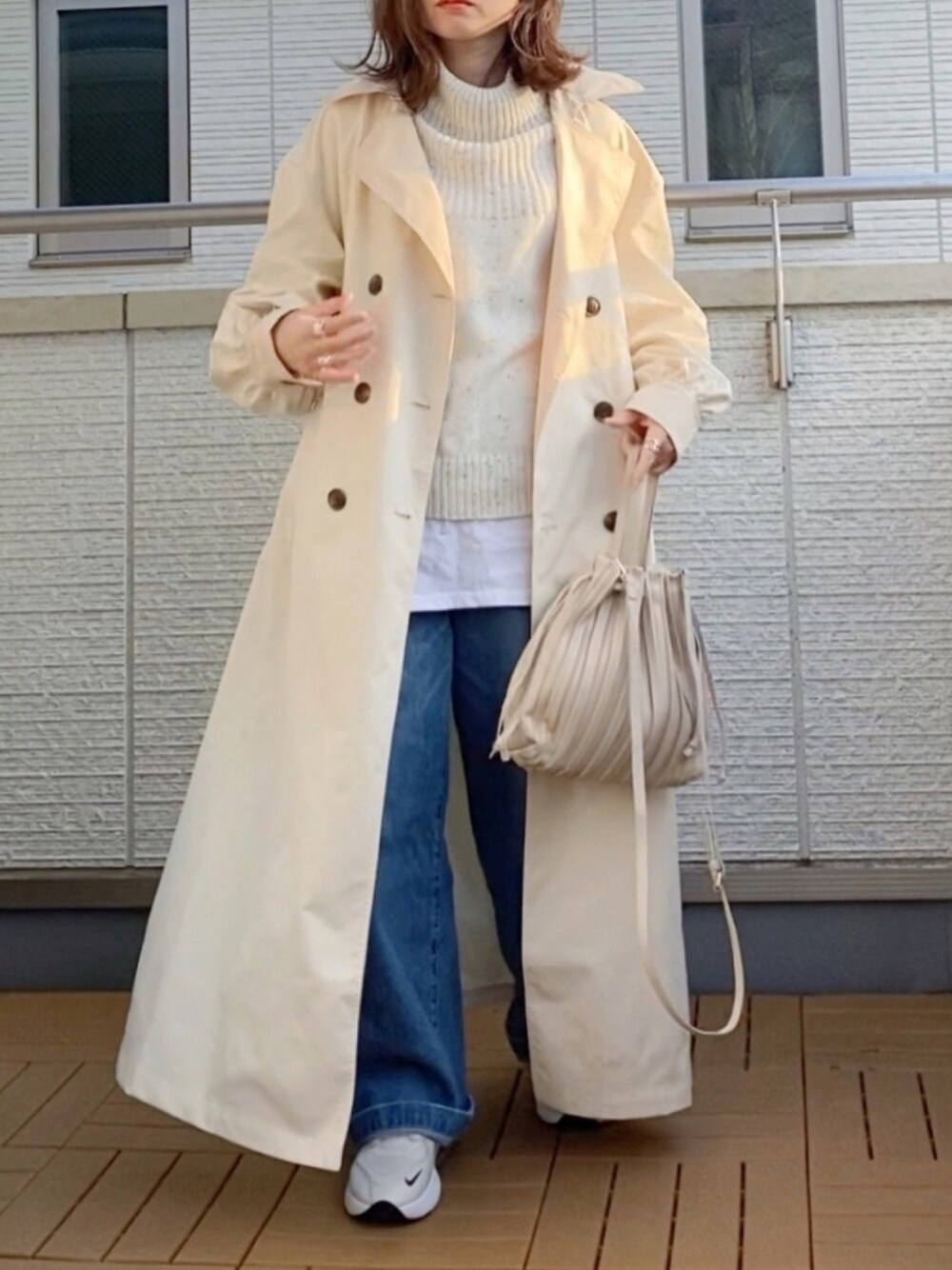 ベージュ系のトレンチコート、ホワイト系のニット/セーター、ブルー系のデニムパンツを着用したレディースの冬コーディネートの1枚目の写真