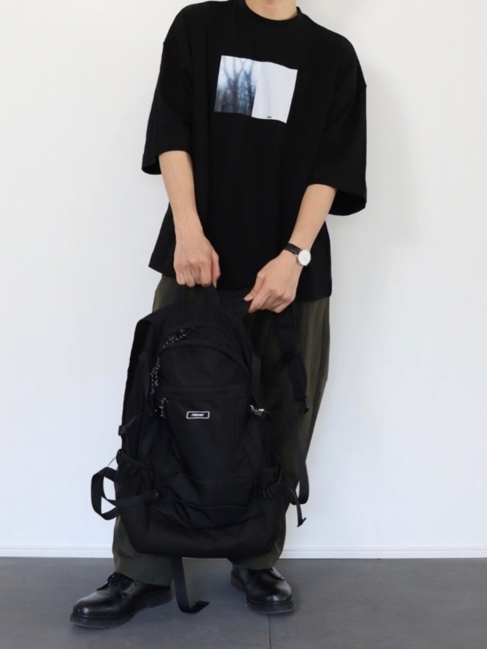 ブラック系のTシャツ/カットソー、ブラック系のバックパック/リュック、グリーン系のその他パンツを着用したメンズの春コーディネートの1枚目の写真