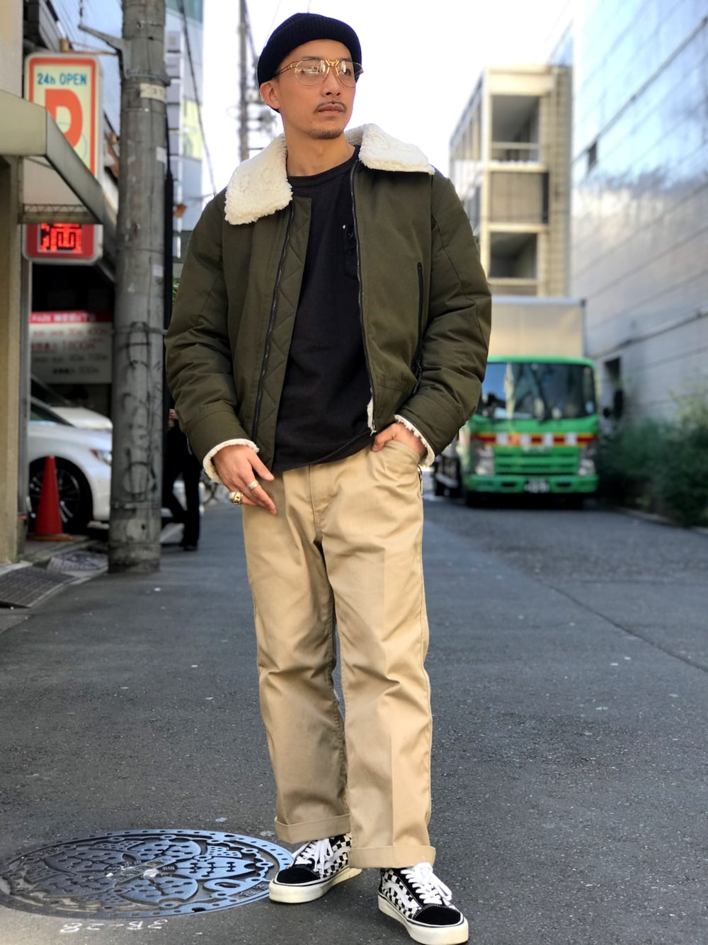 ブラック系のTシャツ/カットソー、ベージュ系のチノパンツ、グリーン系のダウンジャケット/コートを着用したメンズの秋コーディネートの1枚目の写真