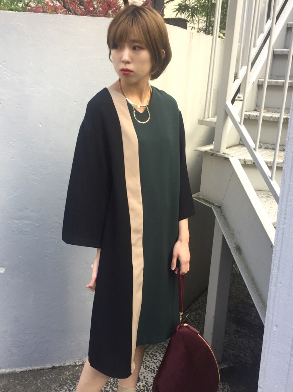 グリーン系のワンピース、レッド系のクラッチバッグを着用したレディースの冬コーディネートの1枚目の写真