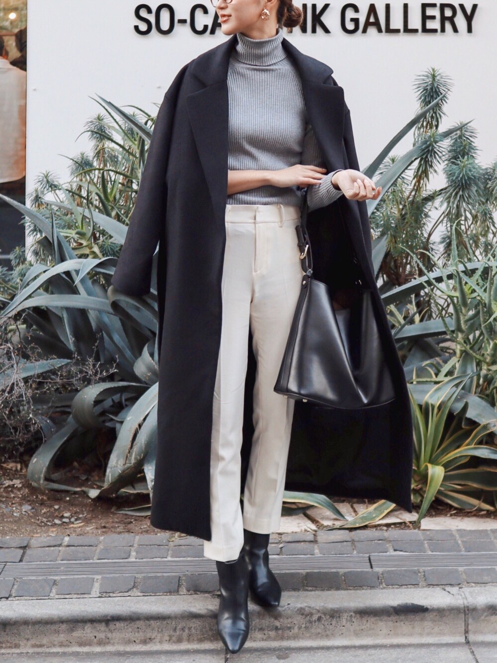 ブラック系のチェスターコート、ホワイト系のデニムパンツ、ブラック系のブーツを着用したレディースの冬コーディネートの1枚目の写真