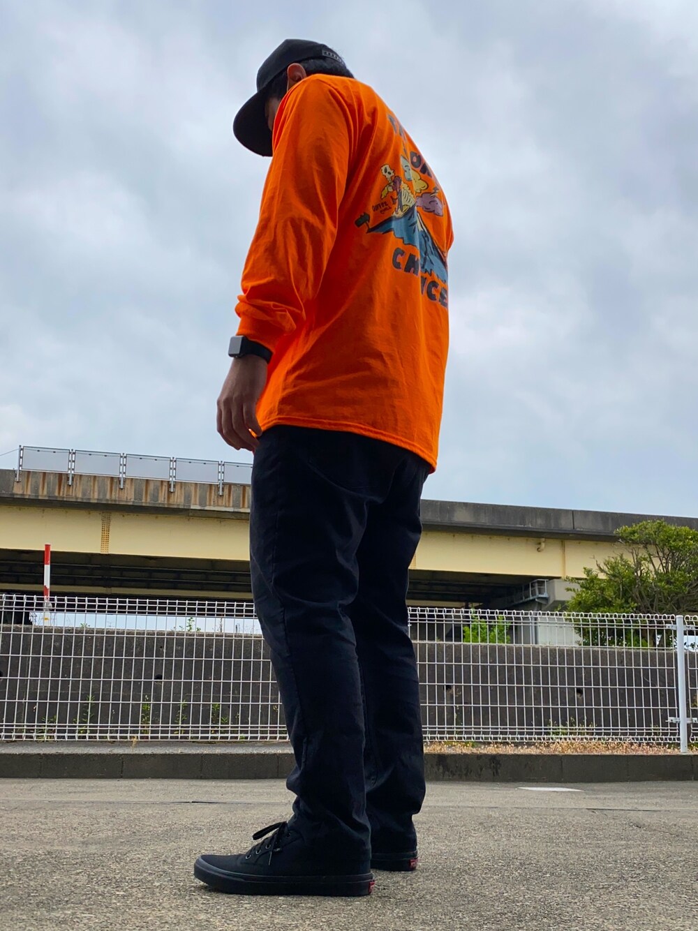 「ロンT、オレンジ、バックプリント、バックスタイル、ﾌﾞﾗｯｸﾊﾟﾝﾂ、キャップ、メッシュキャップ、スニーカー、ブラックスニーカー、ハデ色」｜「THM(THE HARD MAN)のアイテム（キャップ、ブラック系）」を使った、比嘉光さん（メンズ・172cm）の春コーディネートの1枚目の写真
