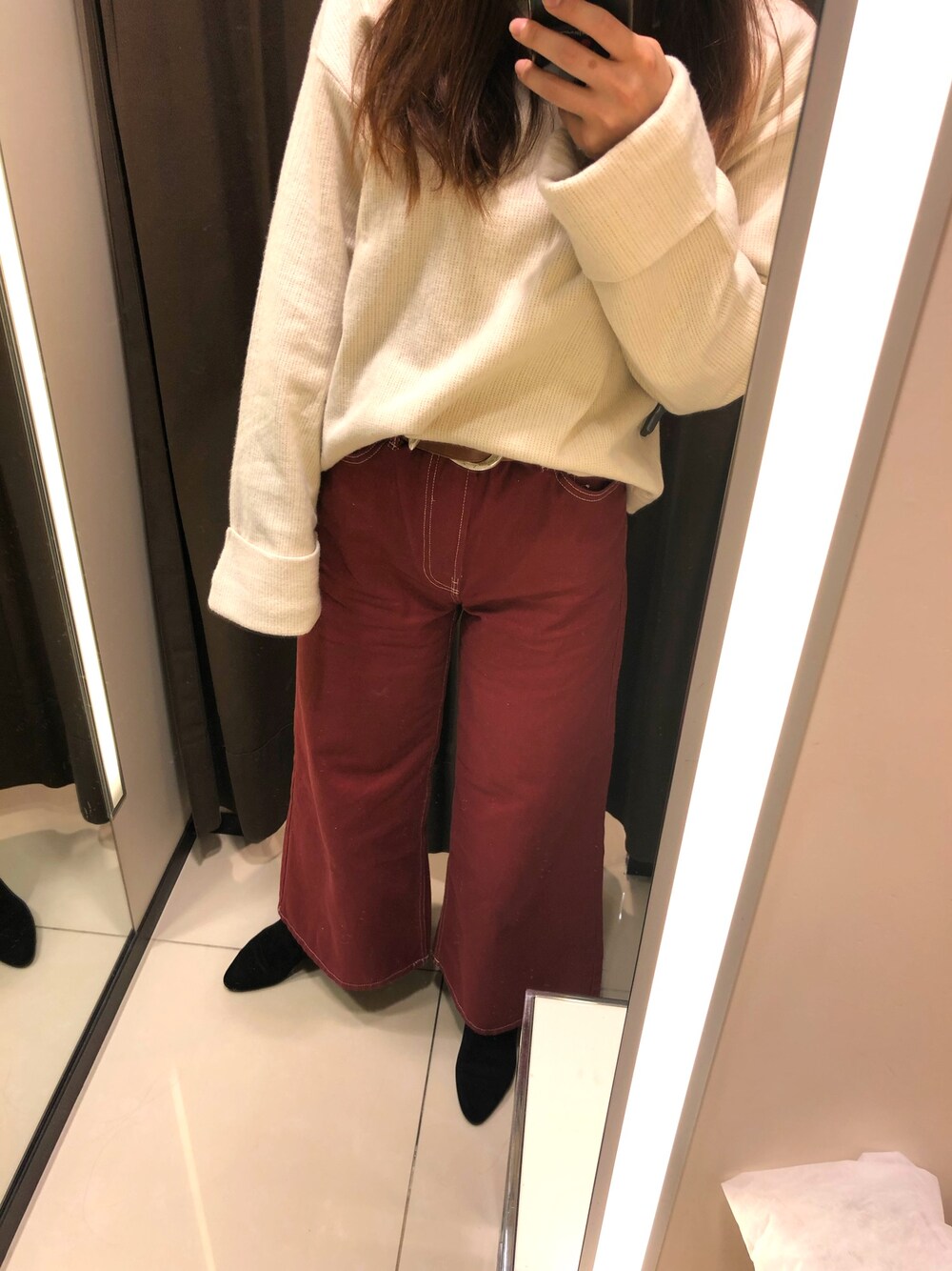 オレンジ系のパンツ、ホワイト系のニット/セーター、ブラック系のブーティを着用したレディースの冬コーディネートの1枚目の写真