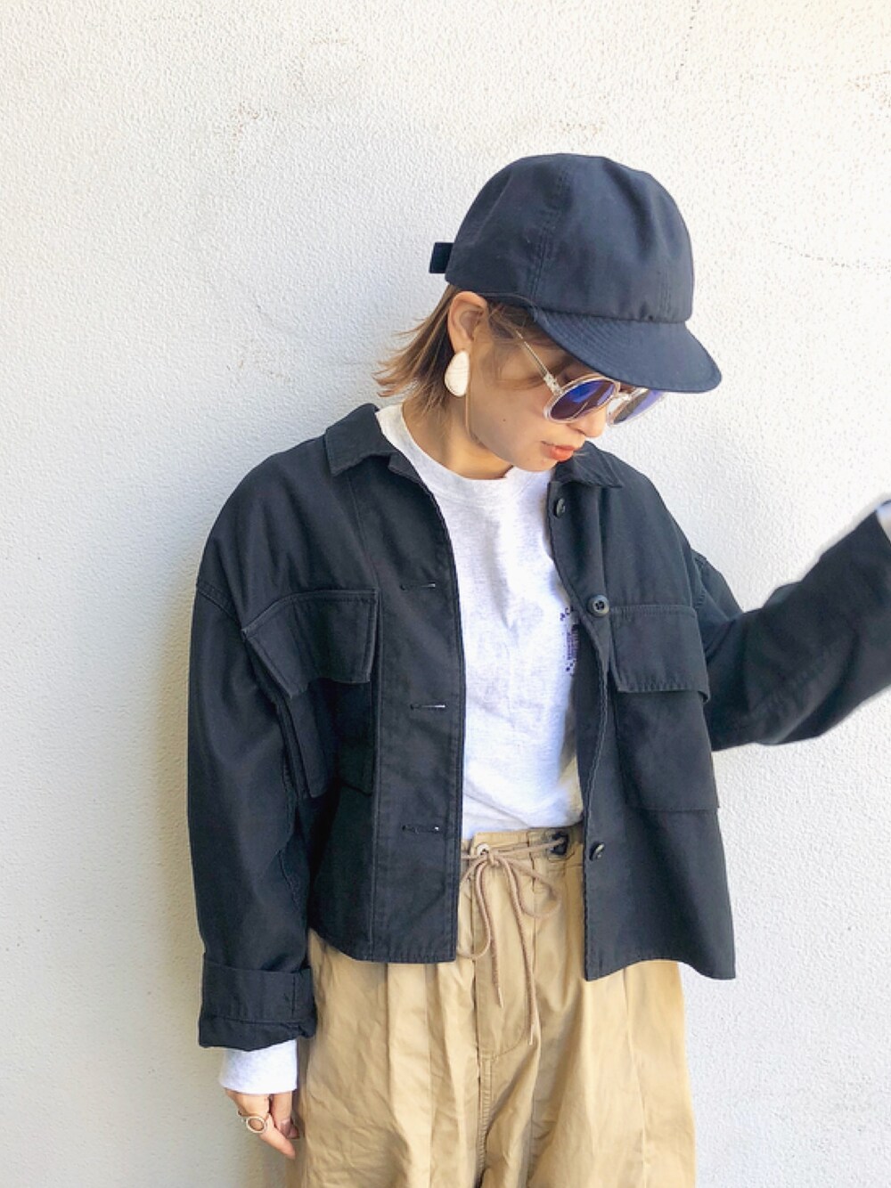 ブラック系のミリタリージャケット、ベージュ系のその他パンツ、ブルー系のキャップを着用したレディースの春コーディネートの1枚目の写真