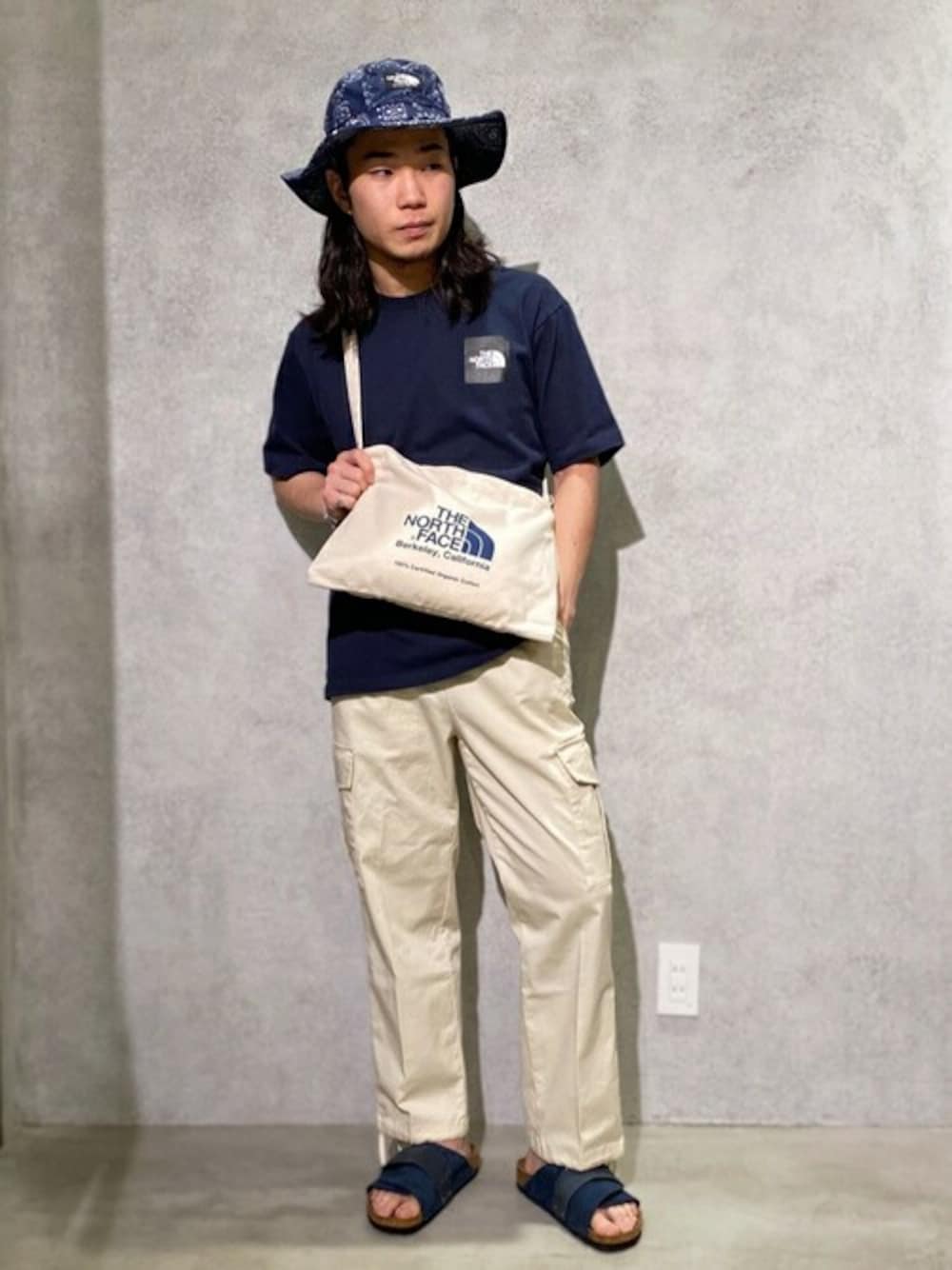 ブラック系のTシャツ/カットソー、ブルー系のサンダル、ブルー系のエコバッグ/サブバッグを着用したメンズの夏コーディネートの1枚目の写真