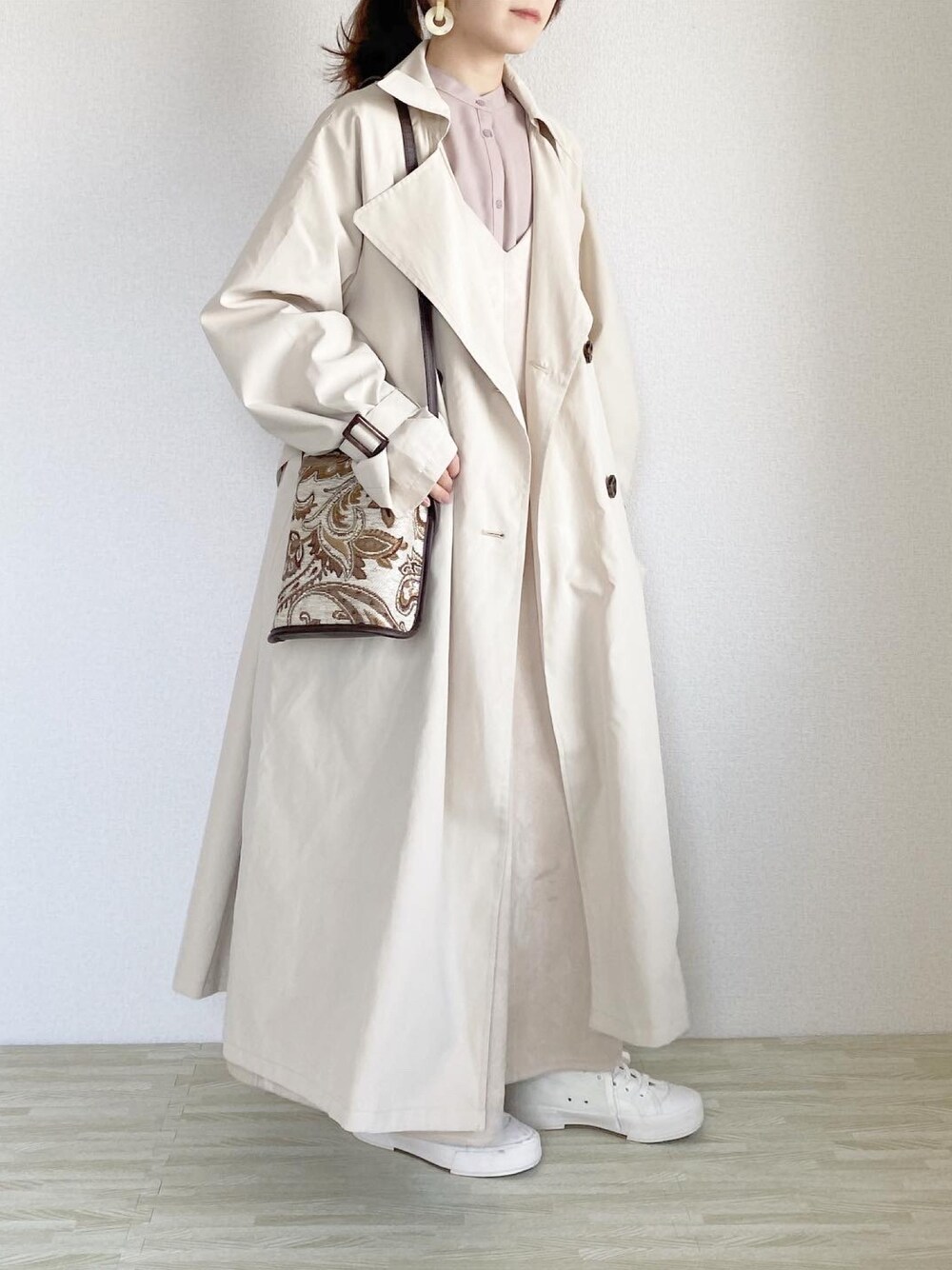 ベージュ系のトレンチコート、ベージュ系のショルダーバッグ、ベージュ系のワンピースを着用したレディースの冬コーディネートの1枚目の写真