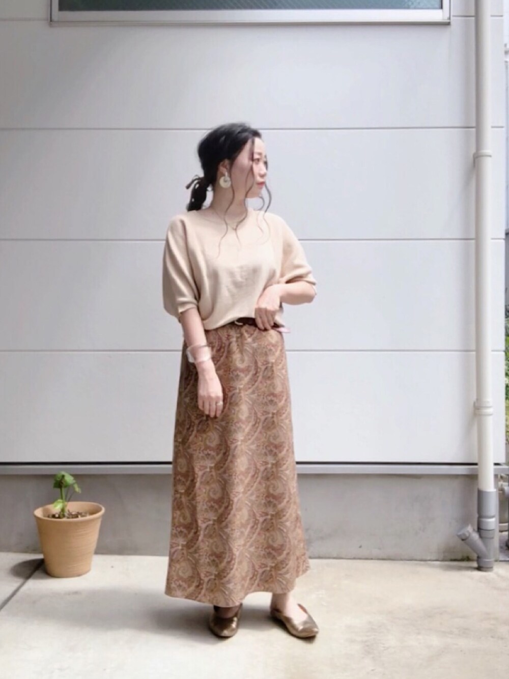 ベージュ系のニット/セーター、ブラウン系のスカート、ゴールド系のパンプスを着用したレディースの夏コーディネートの1枚目の写真