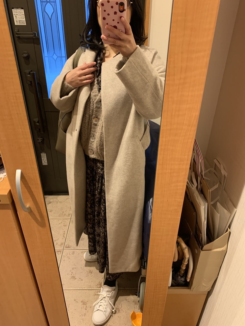 ベージュ系のノーカラーコート、グレー系のカーディガン/ボレロ、ブラウン系のワンピースを着用したレディースの冬コーディネートの1枚目の写真