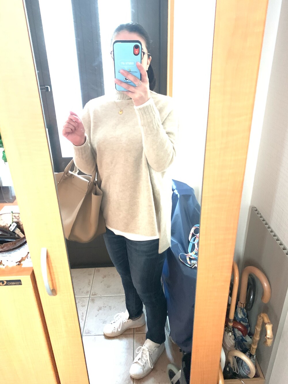 ベージュ系のニット/セーター、ベージュ系のバッグ、ブルー系のデニムパンツを着用したレディースの冬コーディネートの1枚目の写真