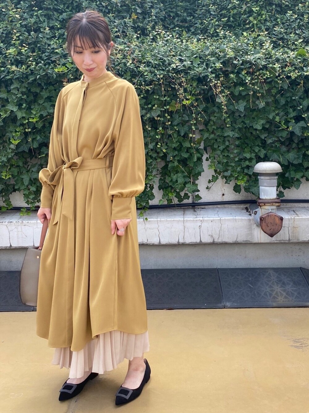 イエロー系のワンピース、ベージュ系のスカート、ブラック系のパンプスを着用したレディースの秋コーディネートの1枚目の写真