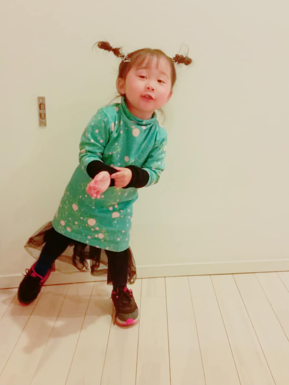 グリーン系のトップス、ブラック系のワンピース/ドレス、ブラック系のシューズを着用したキッズの春コーディネートの1枚目の写真