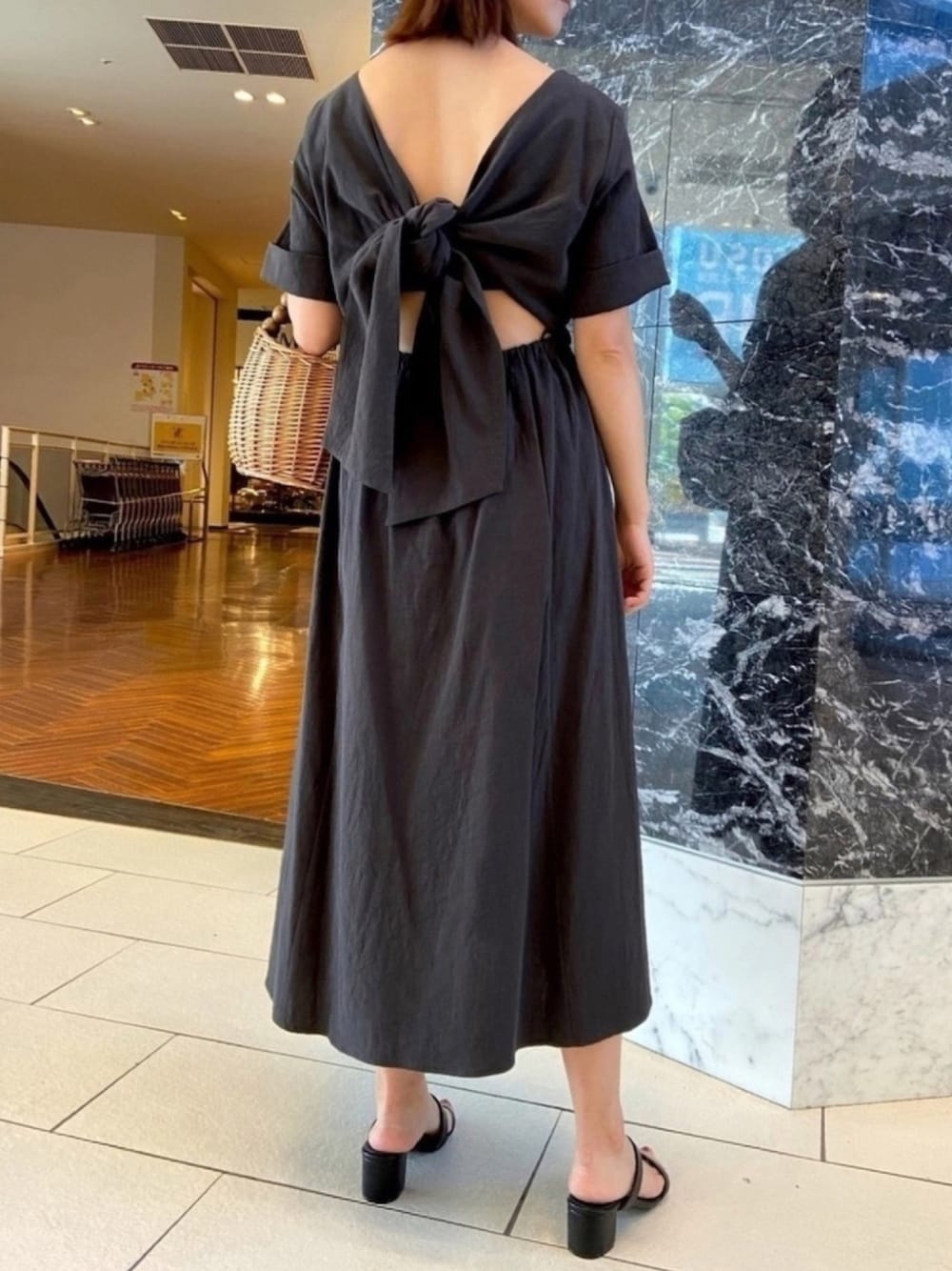 ブラック系のワンピース、ブラック系のサンダル、ブラウン系のかごバッグを着用したレディースの夏コーディネートの1枚目の写真