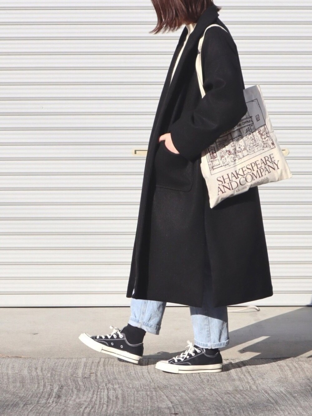 ブラック系のチェスターコート、ホワイト系のニット/セーター、ブルー系のデニムパンツを着用したレディースの冬コーディネートの1枚目の写真